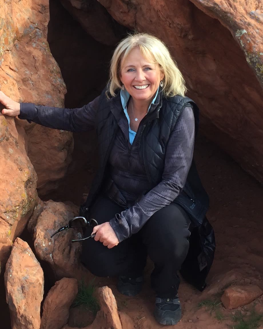 Mare, smiling, kneeling among red sandstone boulders.